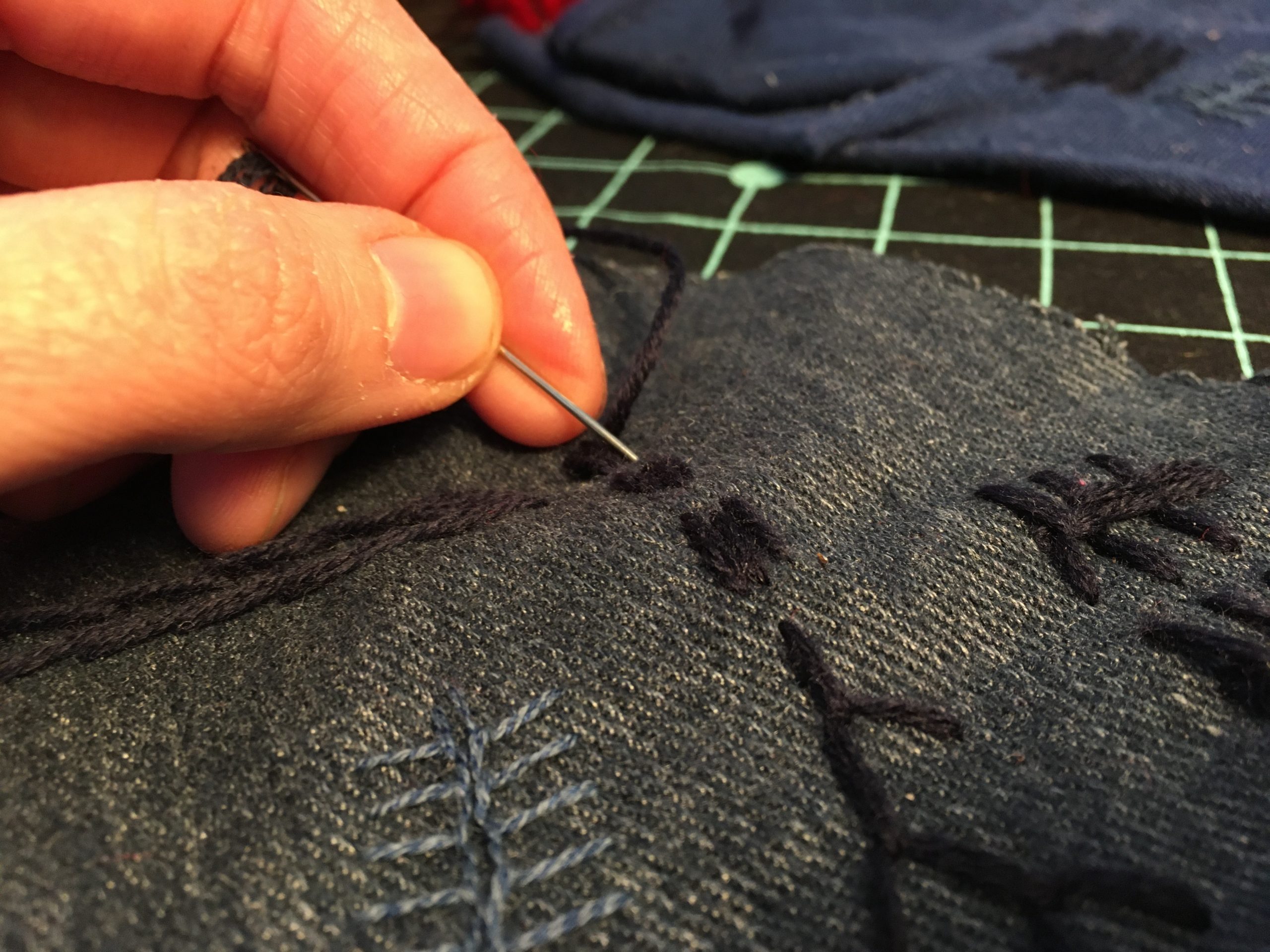 A hand holding a needle and some embroidered fabric