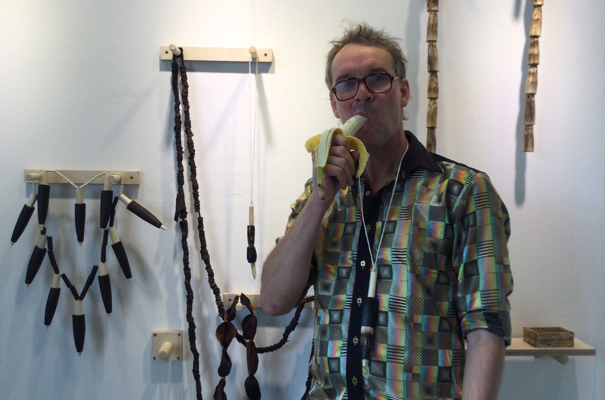 Man eating banana in front of display of large-scale jewellery made from natural materials