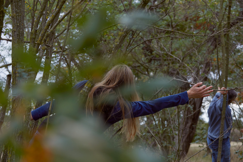 two people with outstretched arms, amongst branches