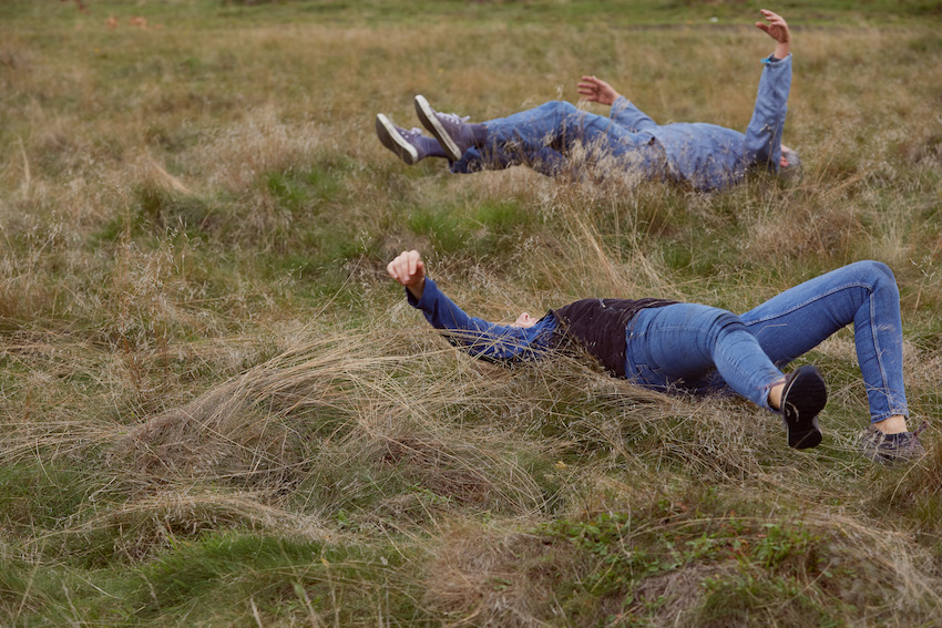 two people lying with outstretched limbs in a grassy landscape