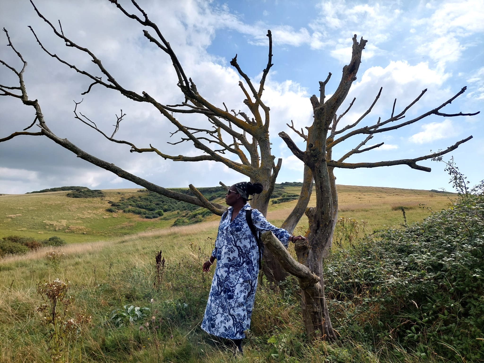 A black woman standing next to a tree in a rural landscape