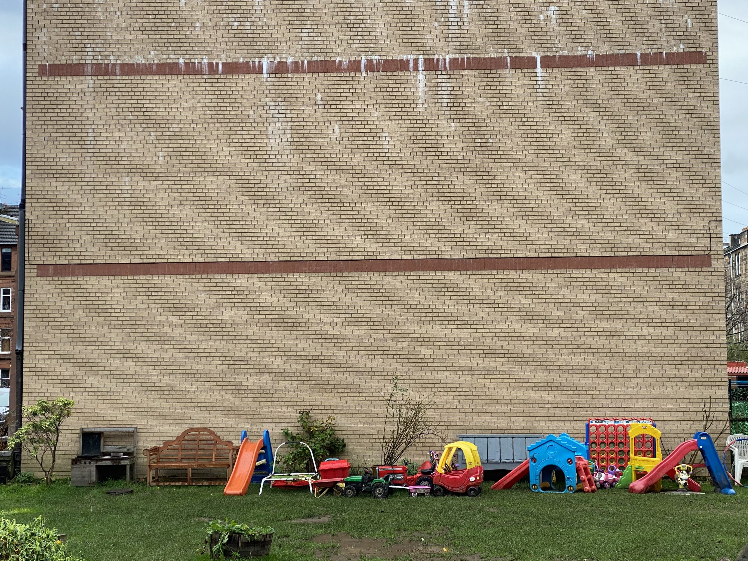 Benches and children's outdoor toys in a garden next to a large wall